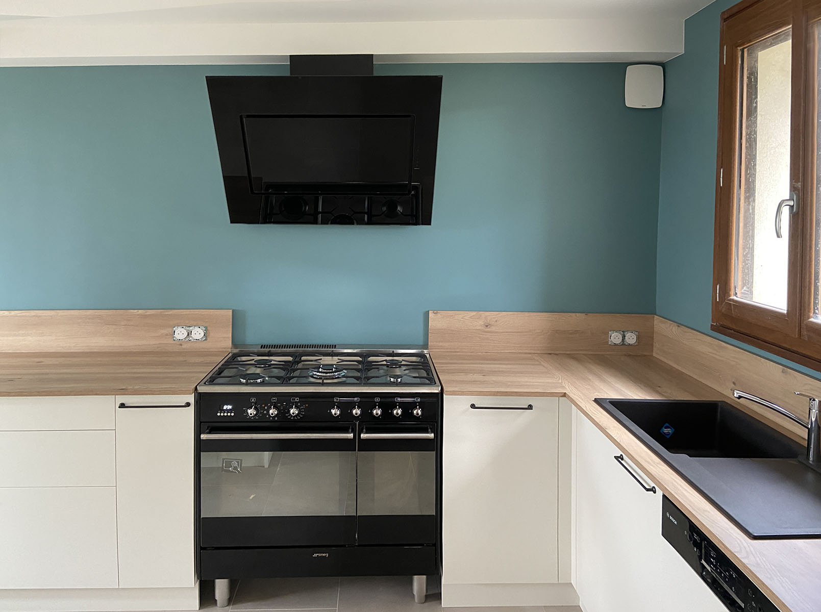 Meubles et Façades — Décor Orgeat Polyrey.
Plan de travail, crédence — Décor chêne des massifs.
Evier — Fragranit Franke®.
Poignées — Laquées noires.
Électroménager — Piano de cuisson, hotte déco.