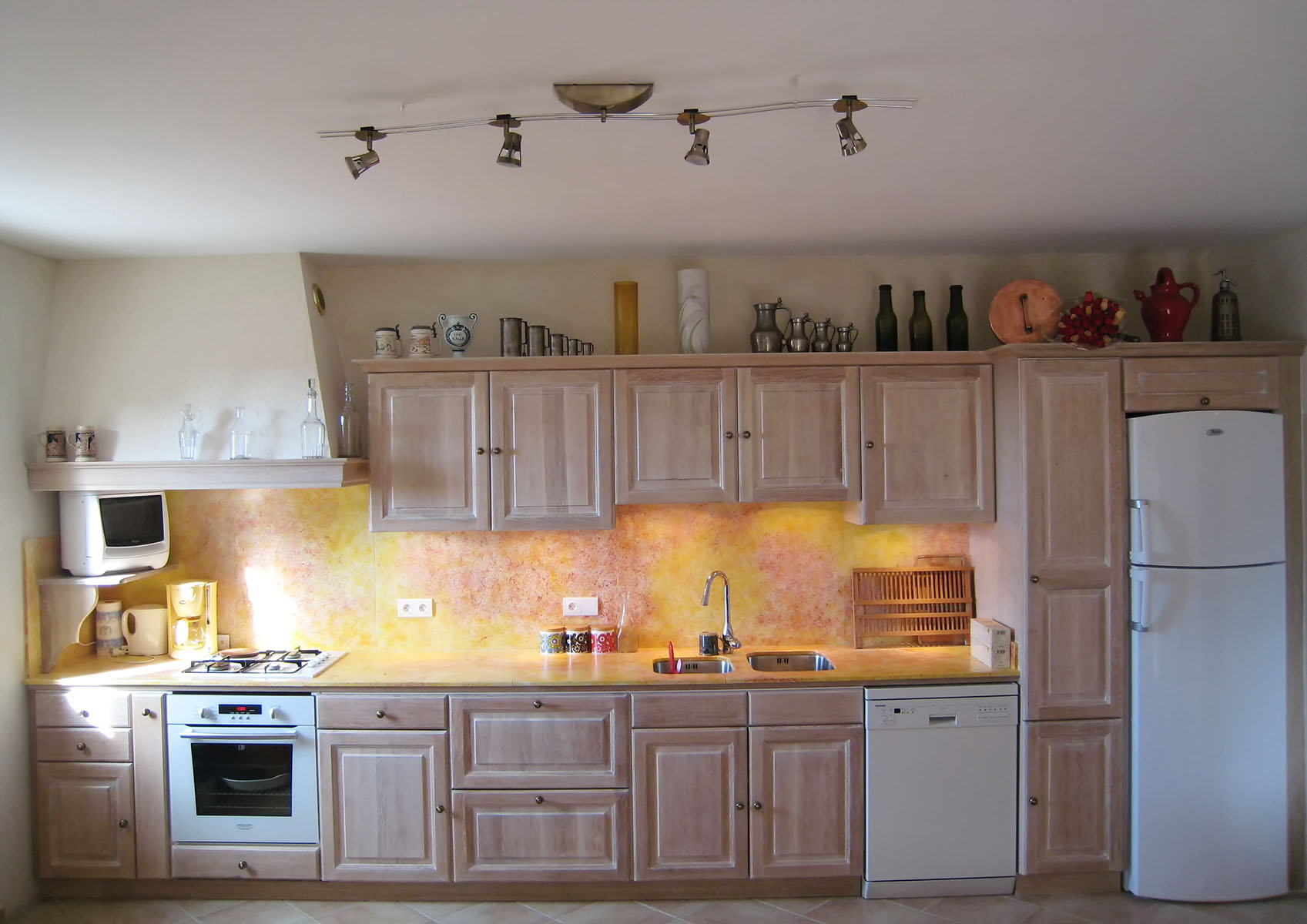 Façades — Chêne massif, cérusé blanc, verni.
Plan de travail, crédence — Lave émaillée.
Évier — Bassin sous plan inox.
Electroménager —  Plaque de cuisson, hotte, four, lave-vaisselle, frigo.