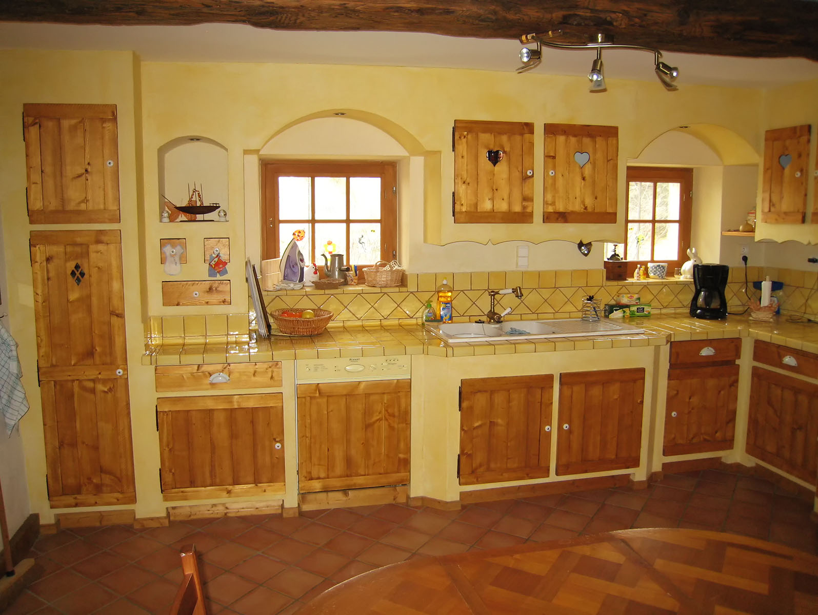 Façade — Epicéa, teinté vernis.
Poignées — Bouton céramique.
Plan de travail et crédence — Carrelage provencale.
Evier — Céramique